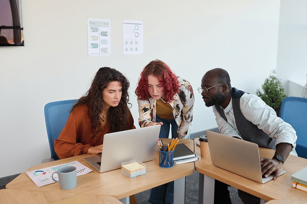 Dos mujeres y un hombre mirando un mismo ordenador en una oficina