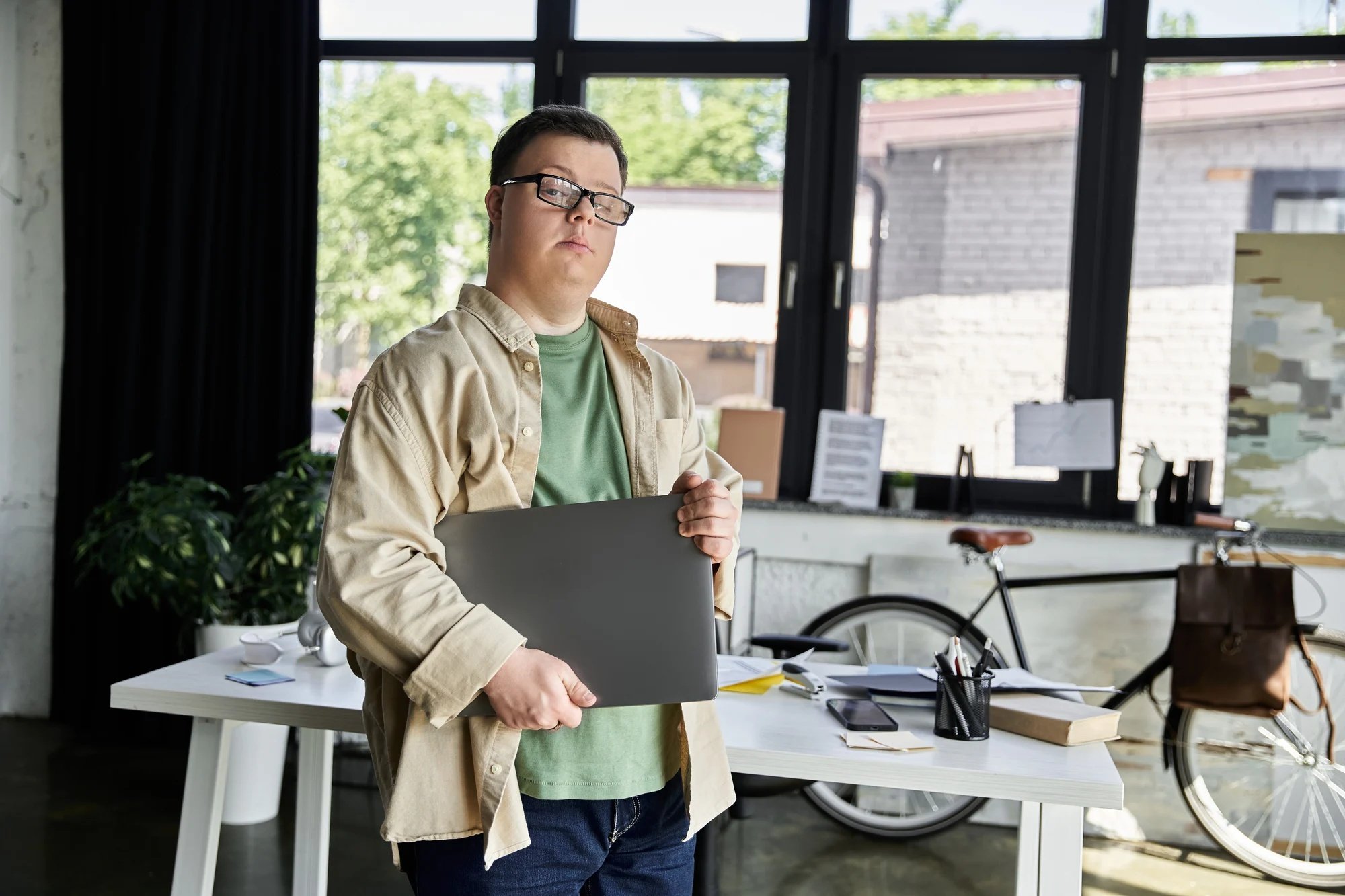 Chico con síndrome de down sosteniendo un ordenador en una oficina